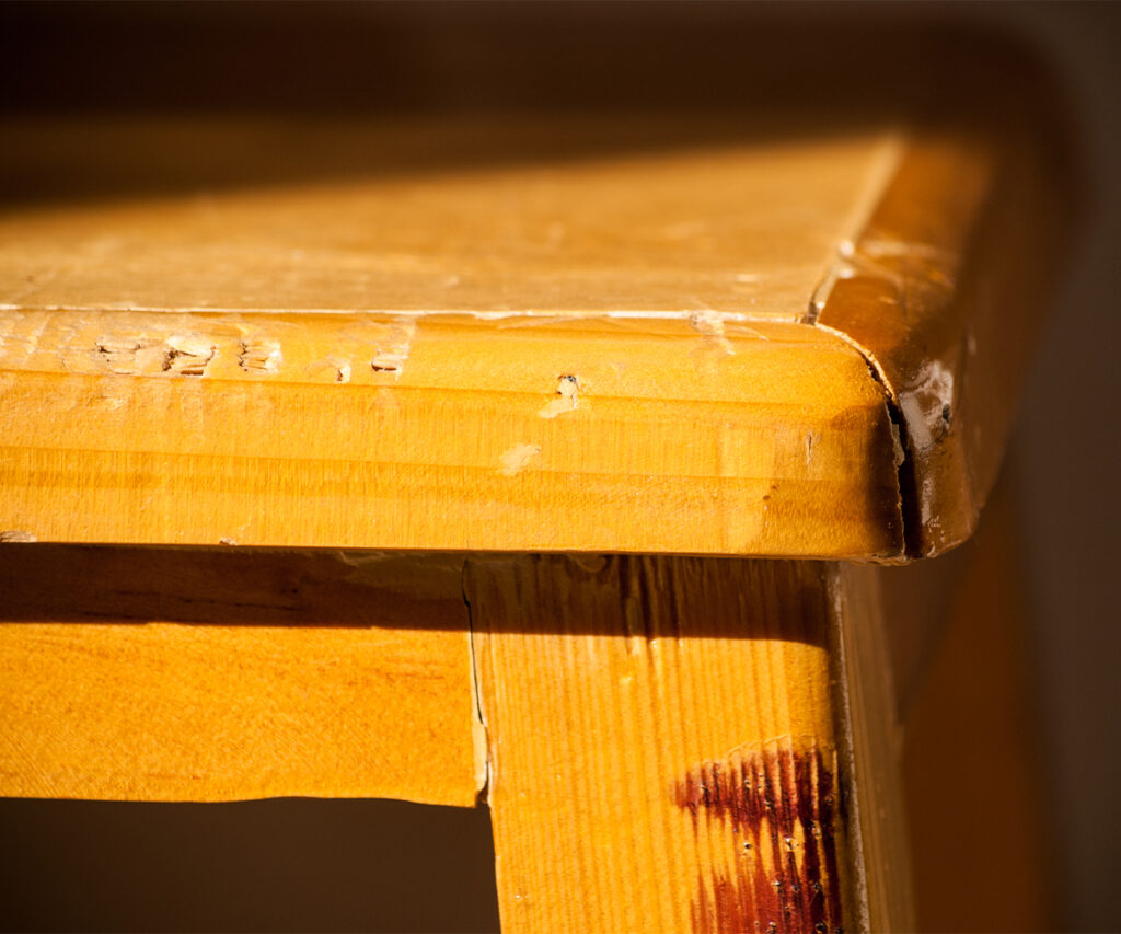 How to care for wood furniture: close-up of a scratched tabletop corner and worn finish.
