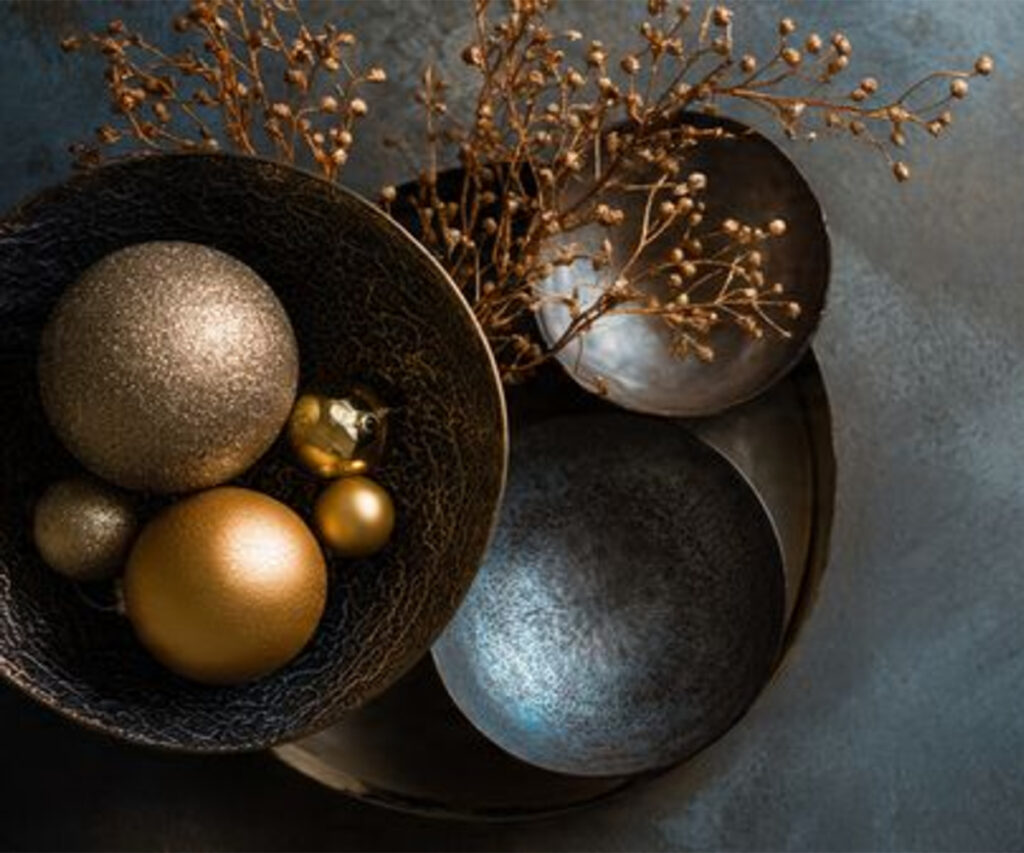 Decorative metal bowls and spheres with branches in gold, bronze, and black tones.