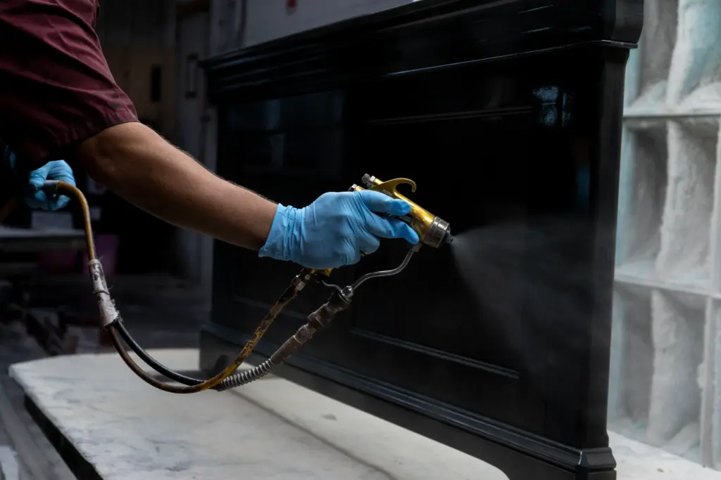Craftsperson applying a dark finish to a wood furniture piece with a spray gun